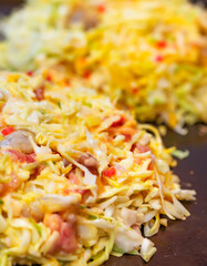 Close-up on an okonomiyaki Japanese pancake or omelet, which means cooked to your liking, prepared with eggs and shredded cabbage with shrimp, squid, onions, pork cooked on a hot plate.