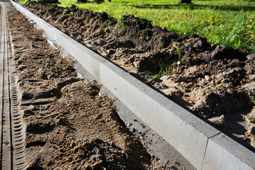 A sidewalk is under construction, a concrete curb is being installed and the foundation of the road is being prepared.