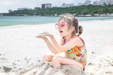 Fototapeta na wymiar A little cute girl with glasses is playing in the sand on the beach by the sea