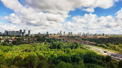 Fototapeta premium Panorama of the city with parks from a height. Blue sky with clouds on buildings under construction.