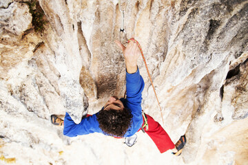 Male rock climber hanging with one hand on challenging route on cliff and putting chalk on another