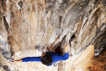 Male rock climber hanging with one hand on challenging route on cliff and putting chalk on another