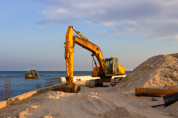 An excavator near the sea digs sand to build a beach on the coastal zone.