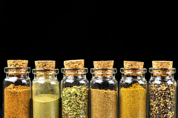 Macro shot of six different spices standing in a vials with a cork, isolated on a black background with space for text at the top.