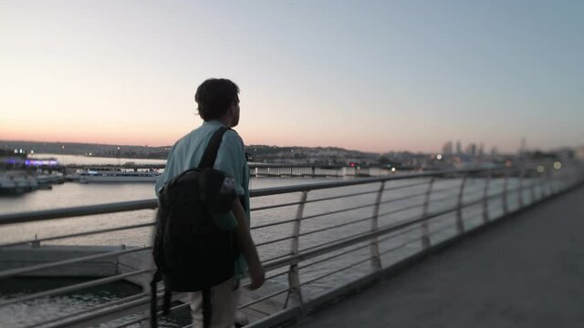 A young handsome guy in a light summer shirt walks over the bridge over the Bosphorus. A tourist with a backpack walks along a bridge, exploring the sights of Istanbul. Turk, Brazilian, Spaniard.