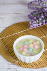 Color rice dumpling in coconut milk (Bua Loy) in white bowl on wooden table with purple flower. Delicious Thai dessert.