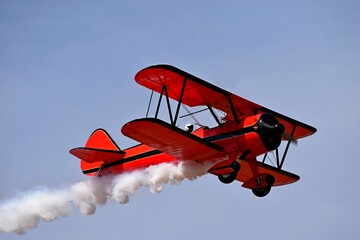 Rode retro vliegtuig (tweedekker) geïsoleerd op blauwe hemelachtergrond. Vintage oude rode vliegtuig &amp  piloot vliegen in de lucht. Mening van rood vliegtuig &amp  witte rook. Dubbeldekker condensatiespoor, rokerig effect na vliegtuig