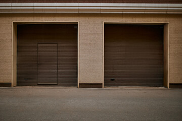 Horizontal shot of corrugated metal doors of garage. Paved road surface and wall with two roller shutters with copy space for your text, information or advertising content. Urban lifestyle