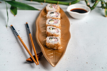 
Sushi on a golden plate in the form of a leaf. Japanese food. Chopsticks, soy sauce on a white plate. Menu cover
