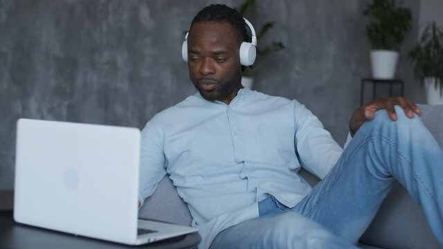 Online education, distance training, business meeting, webinar conference. African American man uses laptop while sitting on sofa
