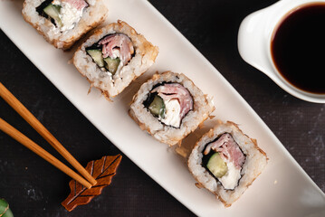 Fresh sushi on white plate. Japanese traditional food. Chopsticks, soy sauce, bamboo branches on black background. Asian style