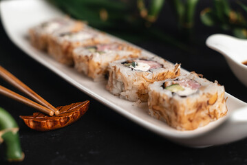 Fresh sushi on white plate. Japanese traditional food. Chopsticks, soy sauce, bamboo branches on black background. Asian style