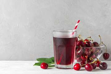 Glass of cold cherry juice with a straw and fresh berries on white background. Refreshment summer drink