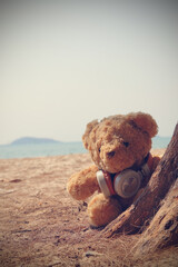 Single brown teddy bear sitting on the beach with headphone. Style retro vintage tone.