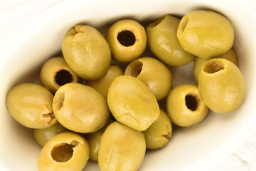 Tinned green pitted olives, close-up, on a wooden table.
