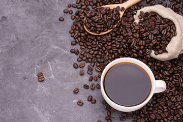 Dark coffee in a white coffee cup with a wooden spoon and roasted coffee beans placed on a black wooden table and there is space for text design.