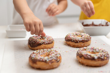 Children decorating doughnuts with colorful sprinkles at home