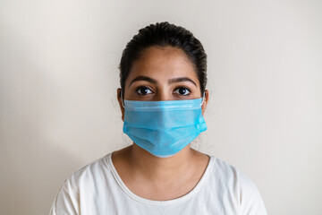 Young Indian woman wearing a protective surgical face mask against white extendable background