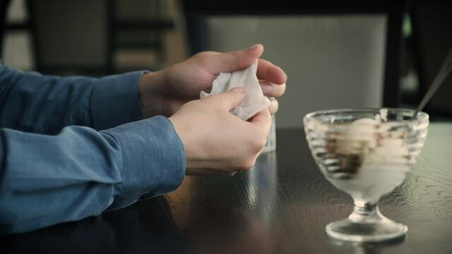 A young man in a cafe before using ice cream thoroughly processes his hands with disinfectants - an antiseptic and wet wipes. Hand hygiene, protection against coronavirus and other diseases.