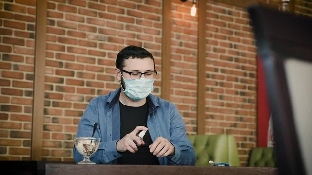 A young man uses hygiene products in a city cafe and without taking off his mask comically eats ice cream.