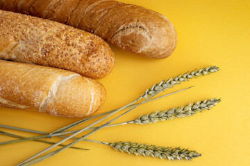Fresh, fragrant baguettes and wheat ears lie on a yellow background. The concept of the grain...