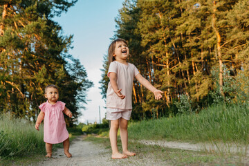 Fototapeta premium Two little sisters of Caucasian appearance play and run barefoot in nature. Concept - friendliness and family interaction between children
