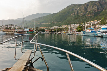 Boat entering Kas harbor at sunset, city with surrounding landscape in a background, Turkey
