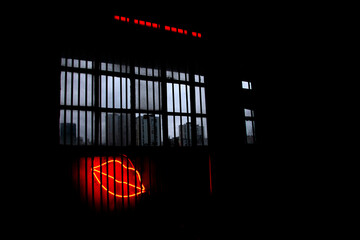 Neon light lips behind bars under a dirty window with a view on cloudy somber cityscape 