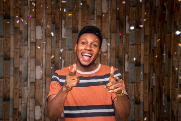 young black man celebrating, with confetti, feeling excited, pointing forward towards camera