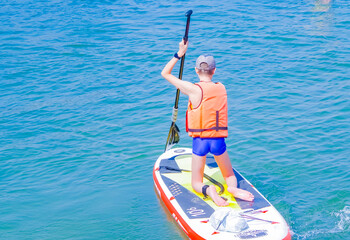 a young rider on a board for Sap surfing rakes a wave with a paddle, the concept of an active...