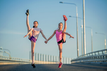 Two teenage girls perform an acrobatic element outdoors against a blue sky	
