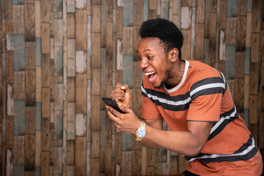 young african man holding his mobile, feeling excited and joyous