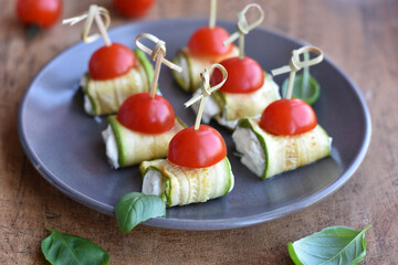 Zucchini appetizer rolls with cream cheese, сherry tomatoes and basil on gray plate. Fried vegetable marrow sushi rolls.