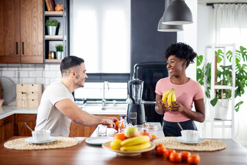 Fototapeta na wymiar Multiethnic couple in the kitchen prepare smoothie with healthy tropical fruits