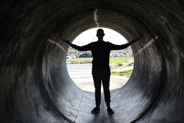 lonely silhouette of a young man in a dark tunnel of a city sewer or drain with backlight....