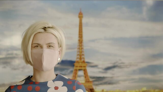 Portrait of a Beautiful Blonde Haired Young Woman Wearing Protective Medical Face Mask and Standing in front of the Eiffel Tower. Safe and Happy Woman Practicing Social Distancing.