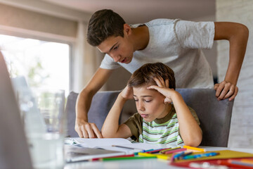 Obraz premium Teenage boy helping his younger brother doing homework at home 