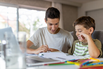 Teenage boy helping his younger brother doing homework at home
