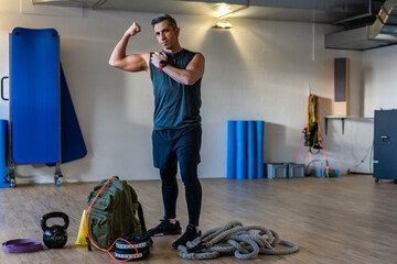 Gym instructor showing muscles. Motivated boot camp instructor stands with gym equipment in gym...