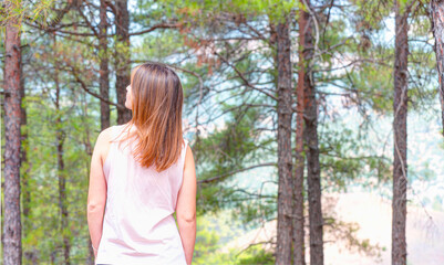 A beautiful young girl stands near an evergreen tree with long green needles