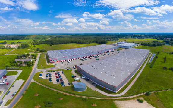 Aerial Top View Of Industrial Storage Building Area With Solar Panels On The Roof And Many Trucks Unloading Merchandise.