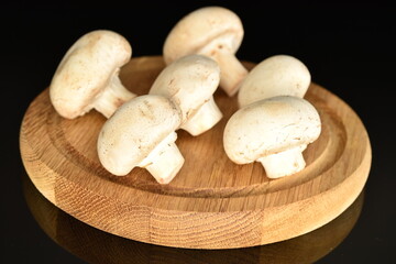 Fresh mushrooms on a wooden board, close-up, on a black background.