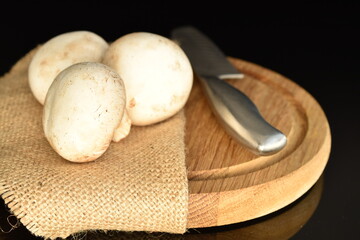 Fresh mushrooms on a wooden board, close-up, on a black background.