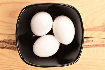 Several chicken eggs in a ceramic plate, closeup, on a wooden table.