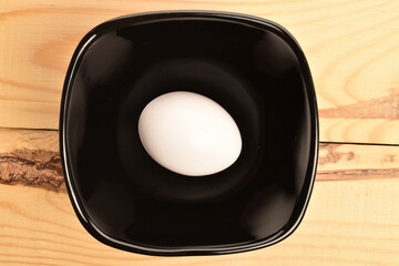 One chicken egg in a black plate, close-up, on a wooden table.
