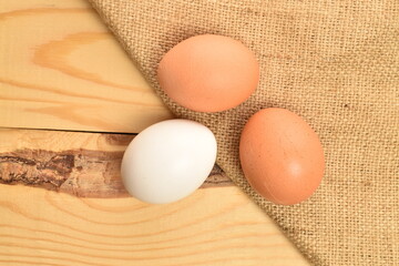 Several chicken eggs with a jute napkin, in a basket, close-up, on a wooden table.