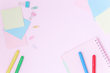 School desk with colorful stationery on pink background.