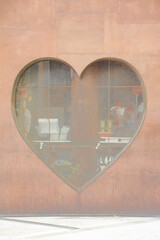 赤茶色の金属のブリキの外壁と、ハートの形の窓枠。縦写真。