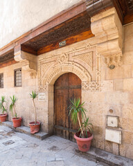Fototapeta na wymiar Angled view of old stone bricks decorated wall with arched wooden door, Entrance of old Ottoman historic house of Moustafa Gaafar Al Selehdar, Moez Street, Old Cairo, Egypt