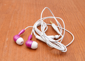 Pink and white earphones on wooden board